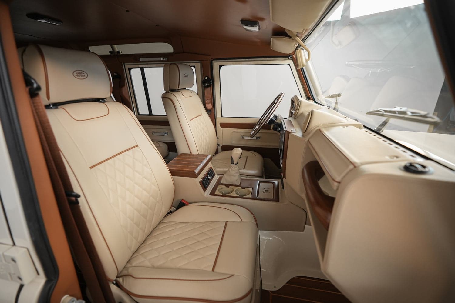 Interior view of a bespoke Land Rover Defender featuring premium beige leather seats with brown accents and wood trim