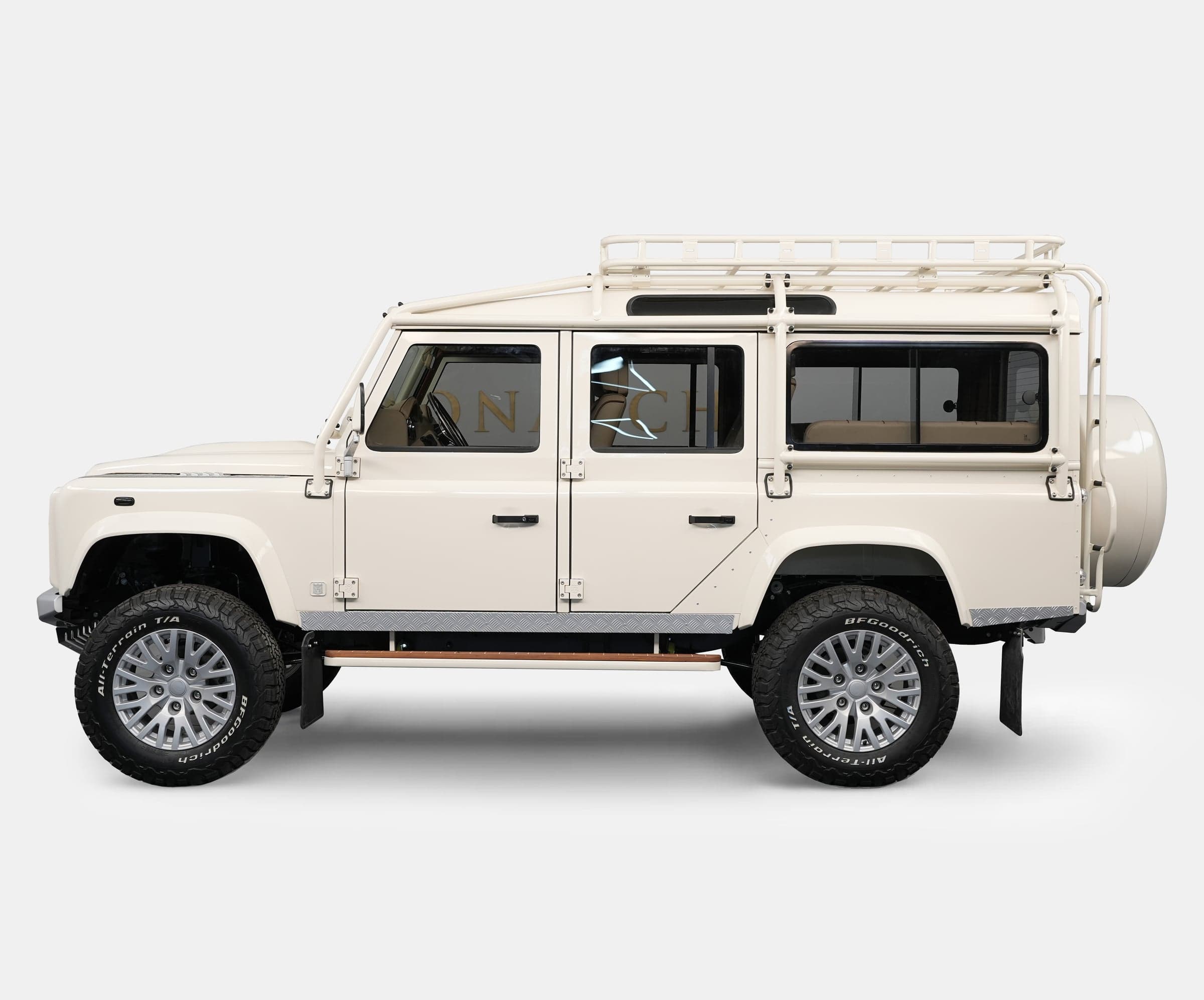 Side view of a bespoke Land Rover Defender in cream color with a roof rack and luxury wheels