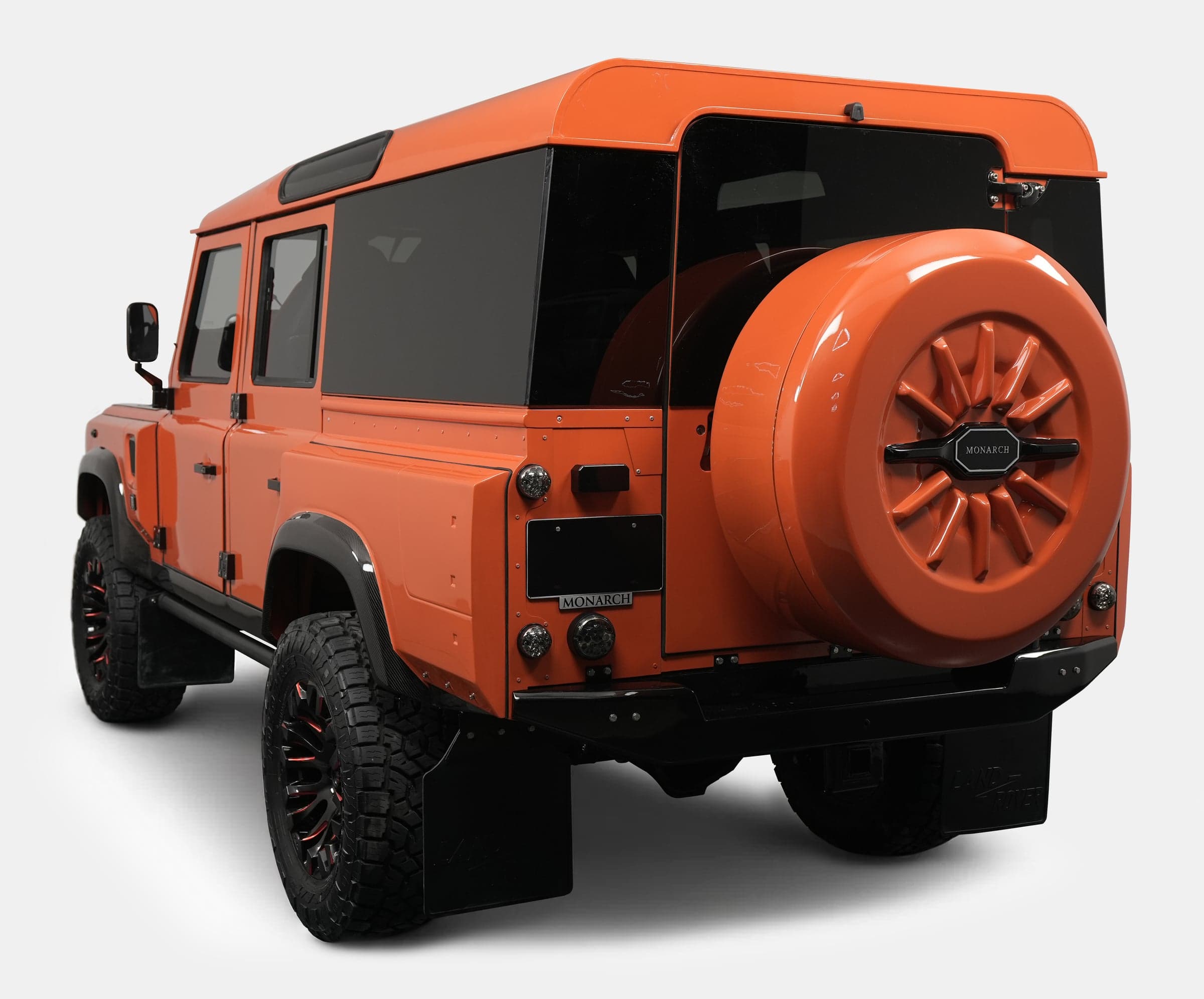 Rear view of a custom orange Land Rover Defender with black accents and unique wheel design