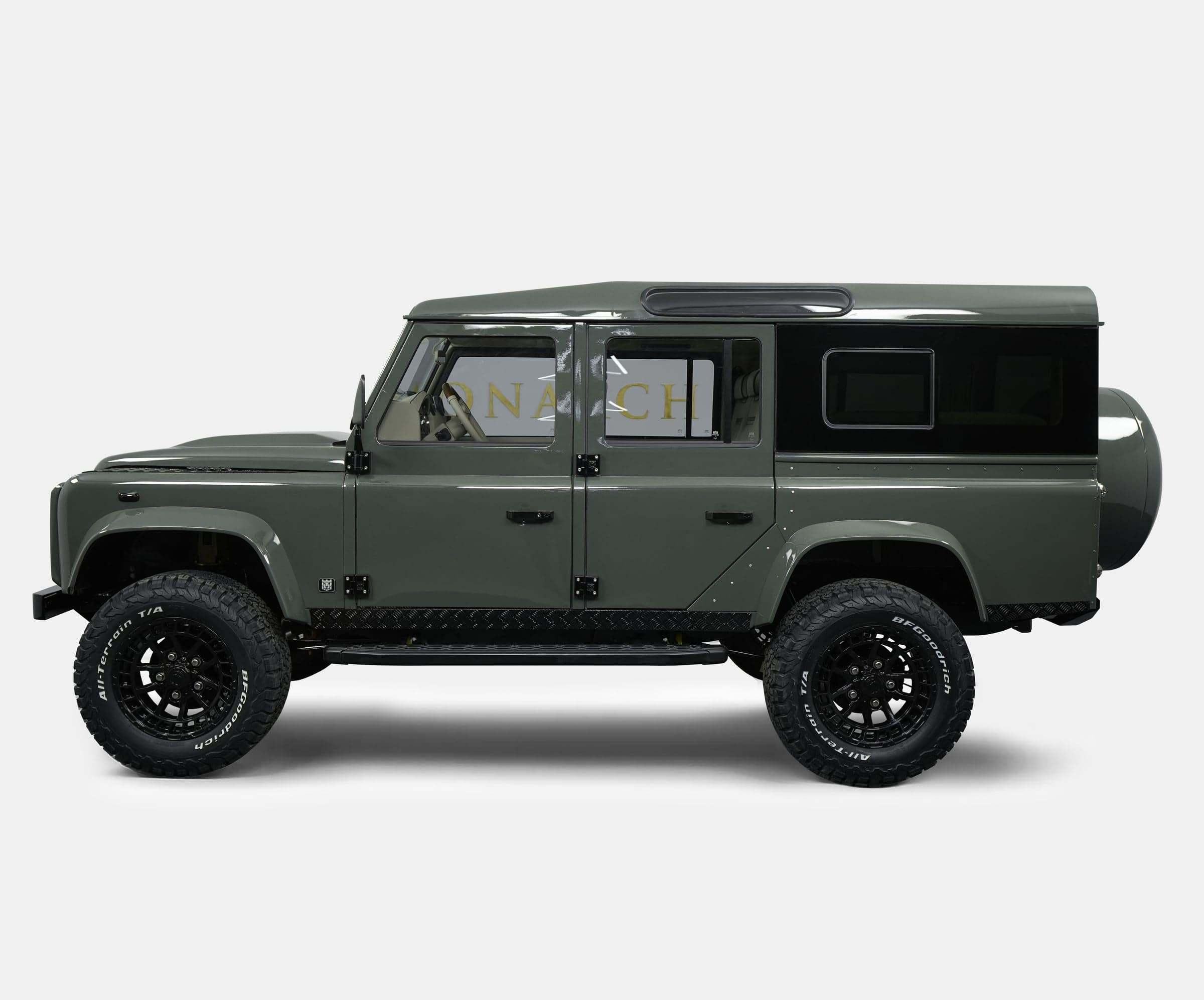 Side view of a custom Land Rover Defender in olive green with black accents and off-road tires