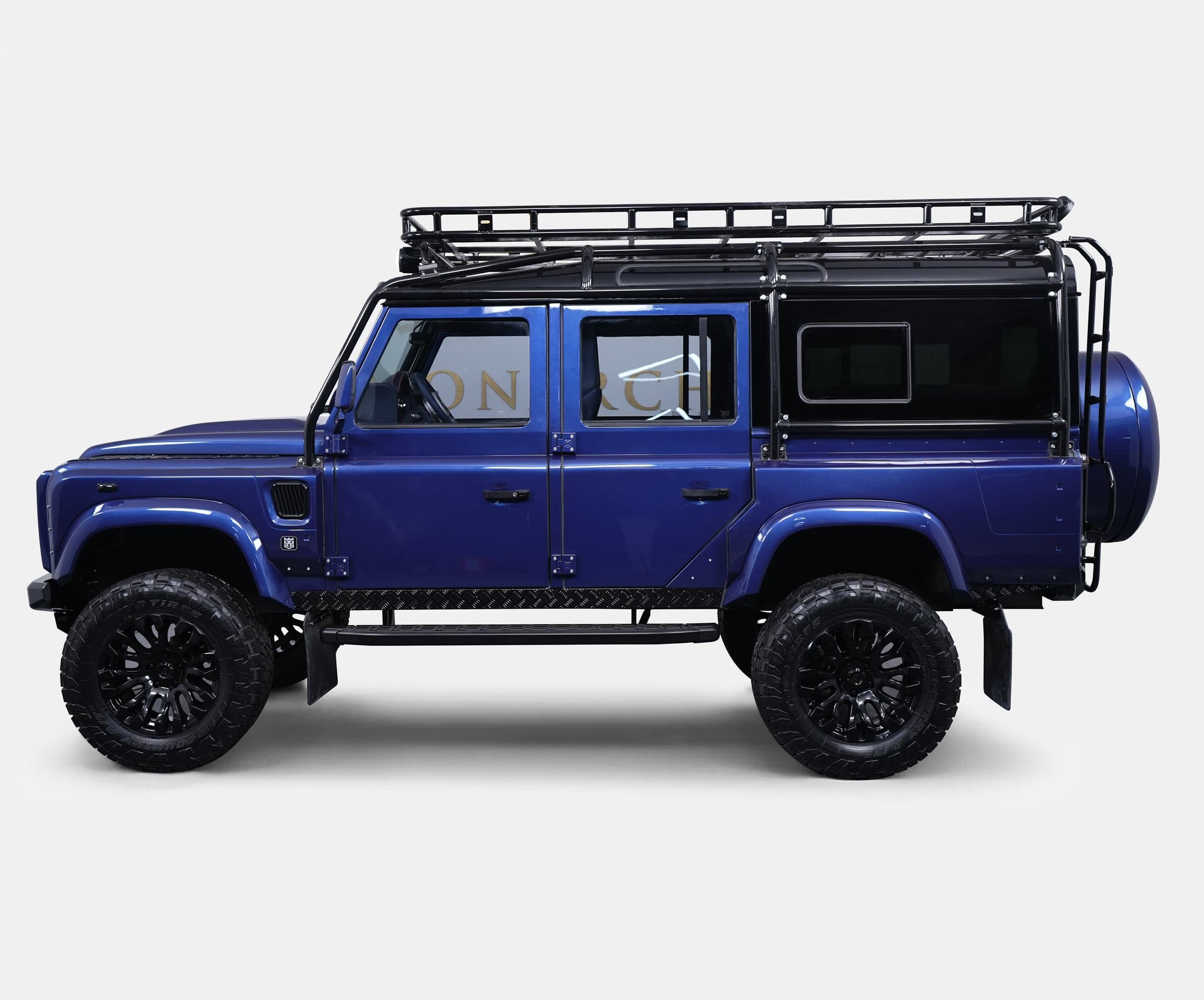 Side view of a bespoke blue Land Rover Defender with black alloy wheels and roof rack