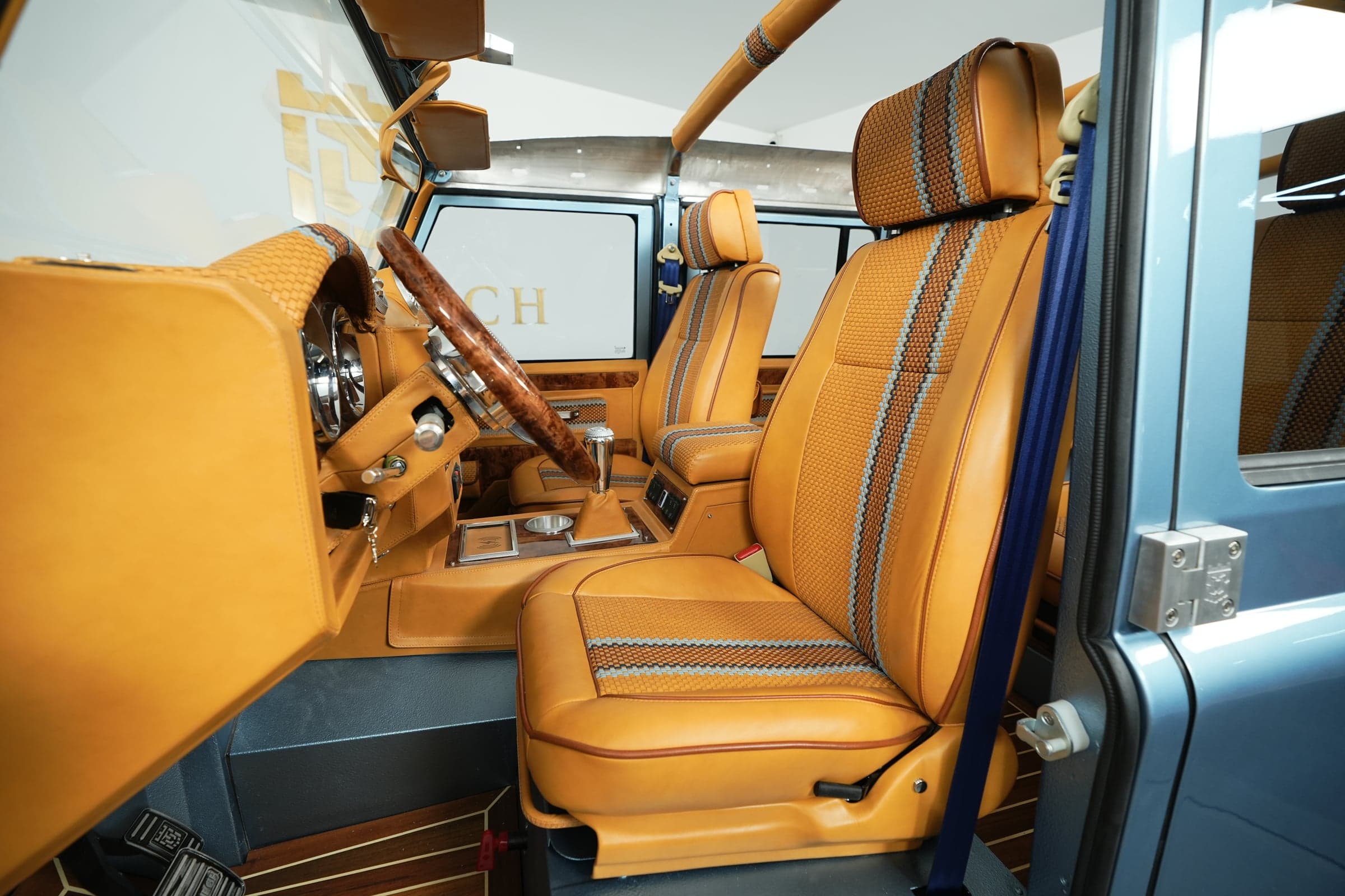 Interior of a bespoke Land Rover Defender featuring tan leather seats with blue accents