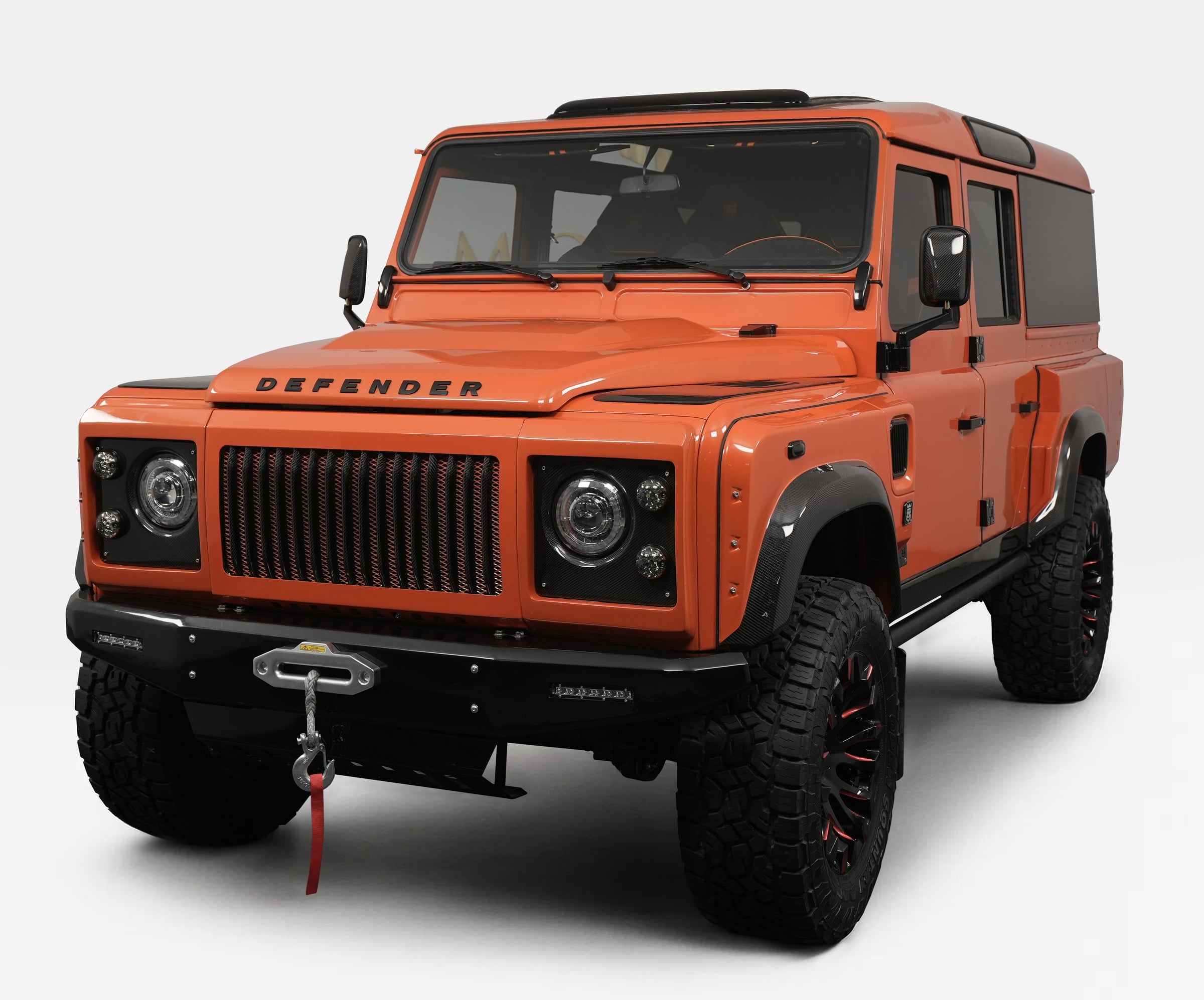 Custom Land Rover Defender in vibrant orange color with rugged tires and off-road features