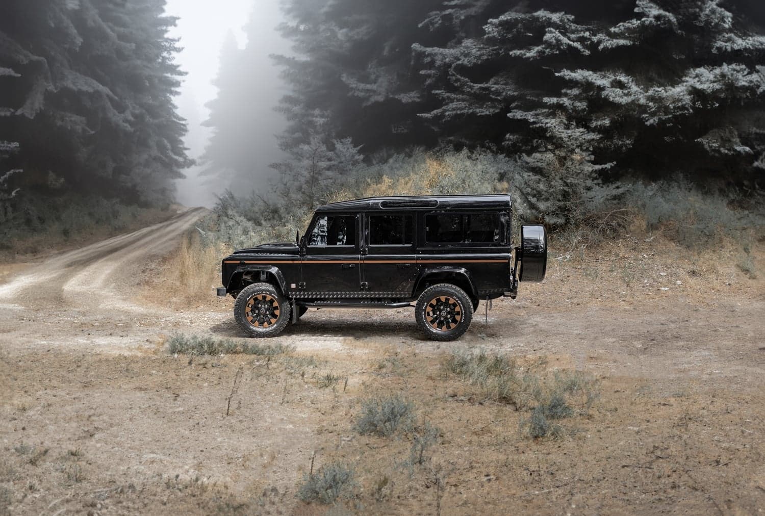 Side View: Bespoke Land Rover Defender Custom Land Rover Defender parked on a dirt road in a misty forest