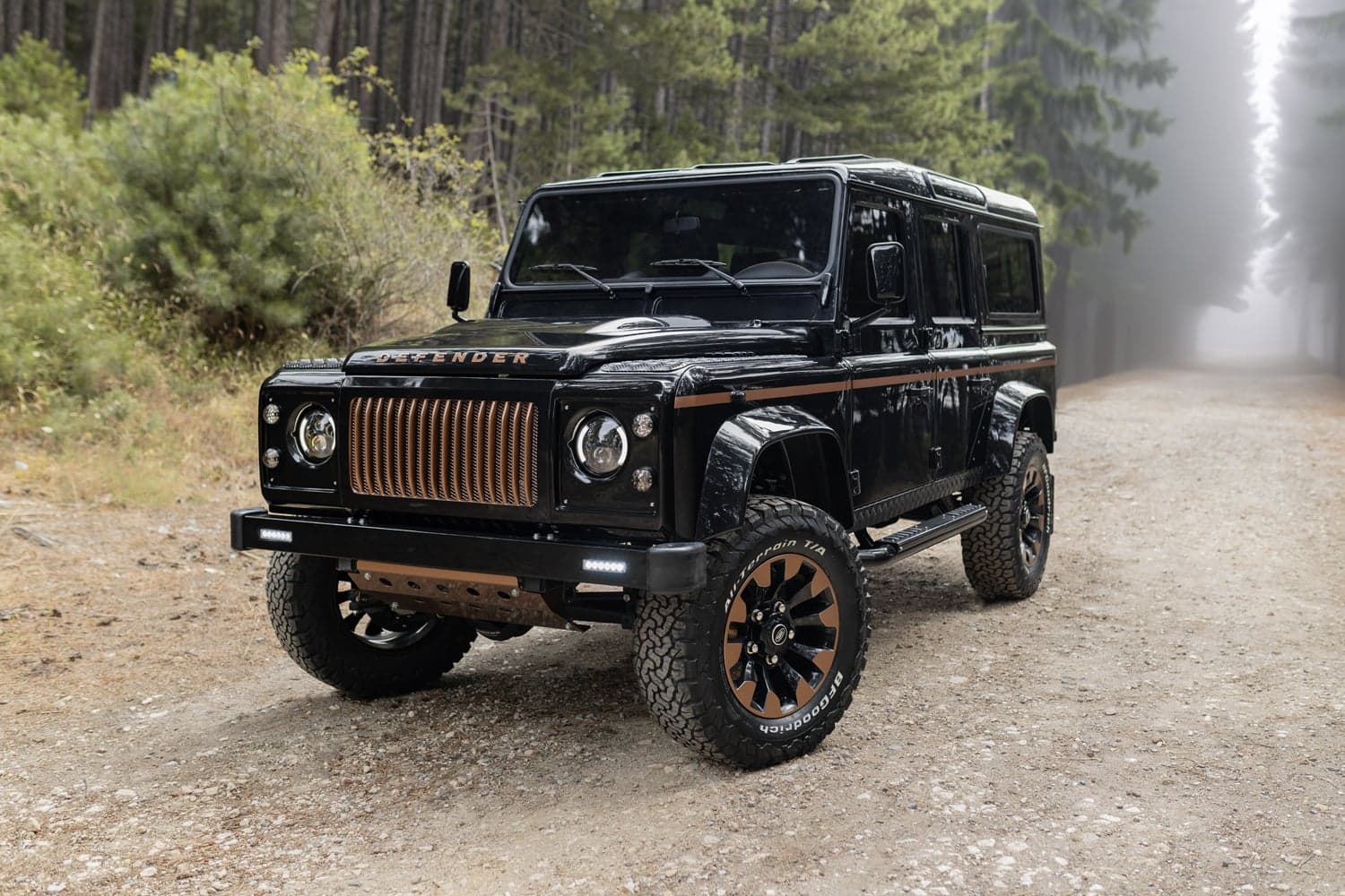Front View: Bespoke Land Rover Defender Custom black Land Rover Defender with bronze accents parked on a forest road
