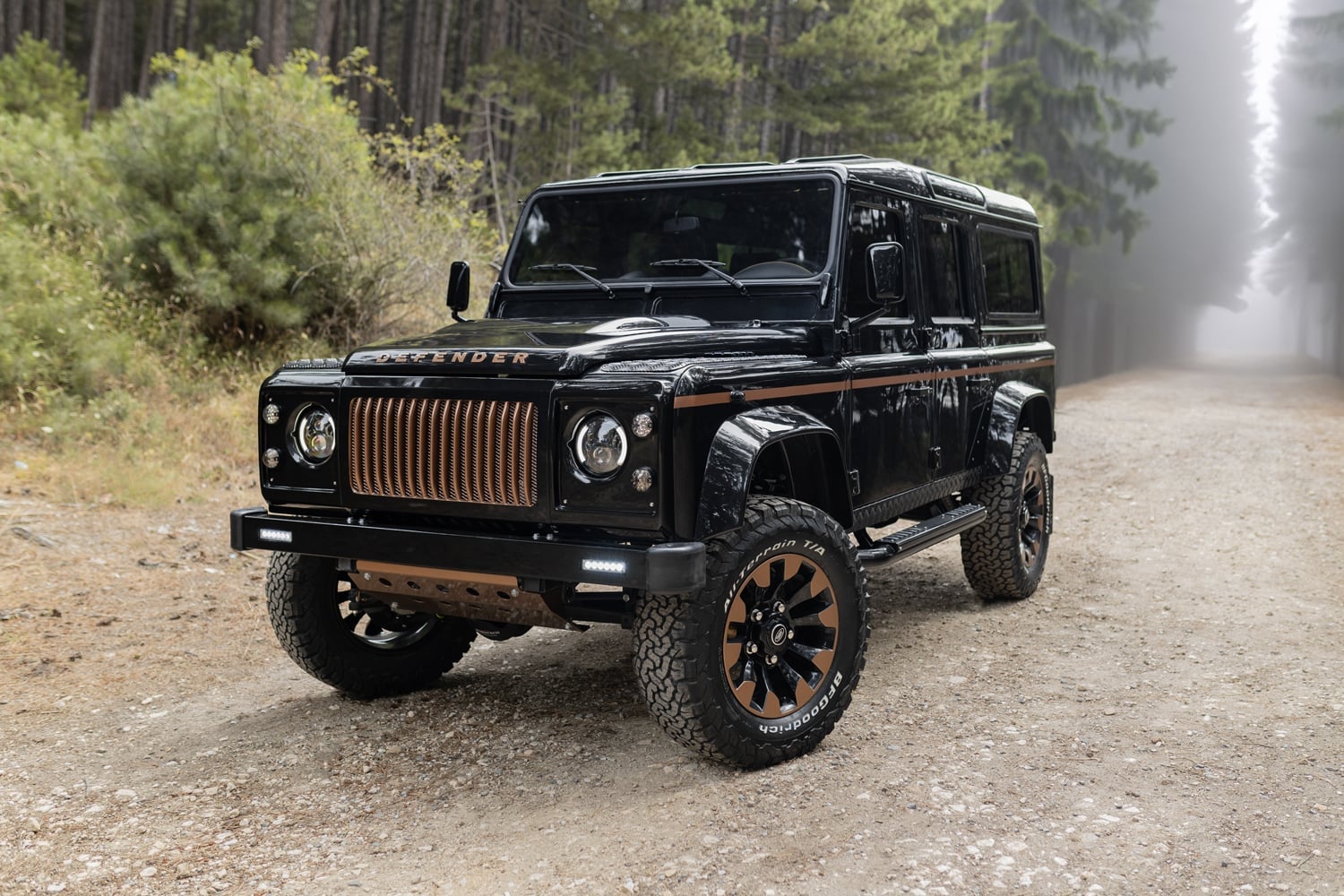 Front View: Bespoke Land Rover Defender Custom black Land Rover Defender with bronze accents parked on a forest road