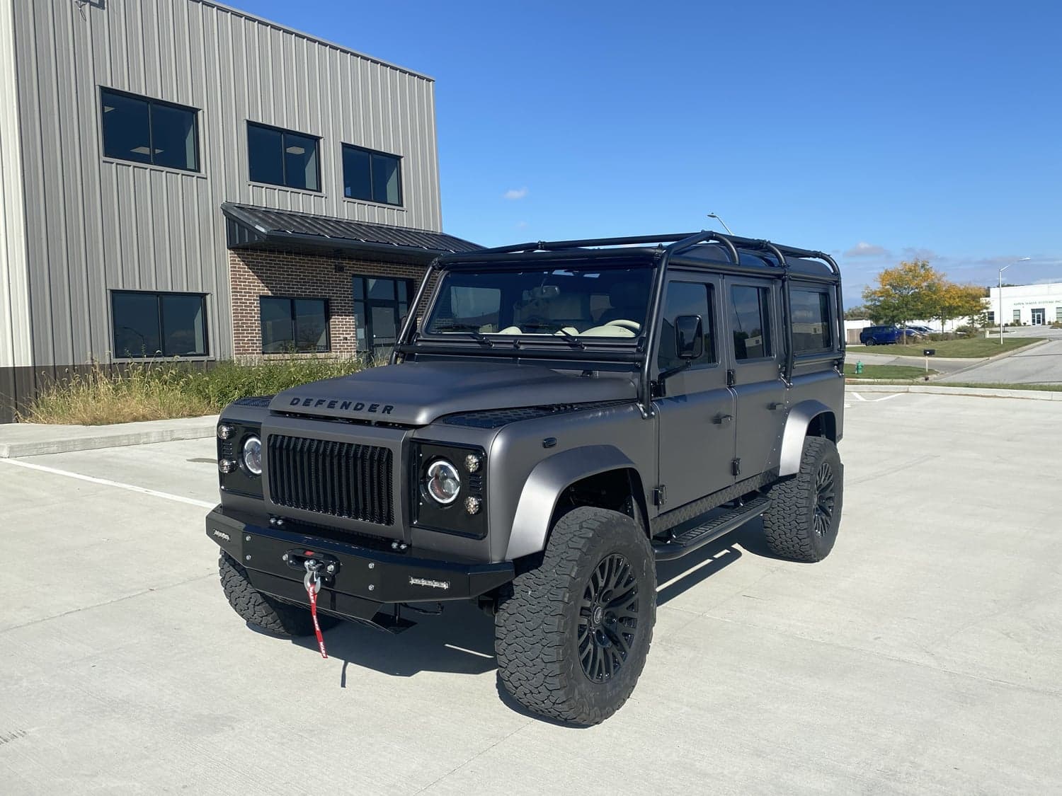 Front View: Bespoke Land Rover Defender Custom Land Rover Defender in matte black finish parked outside a modern building