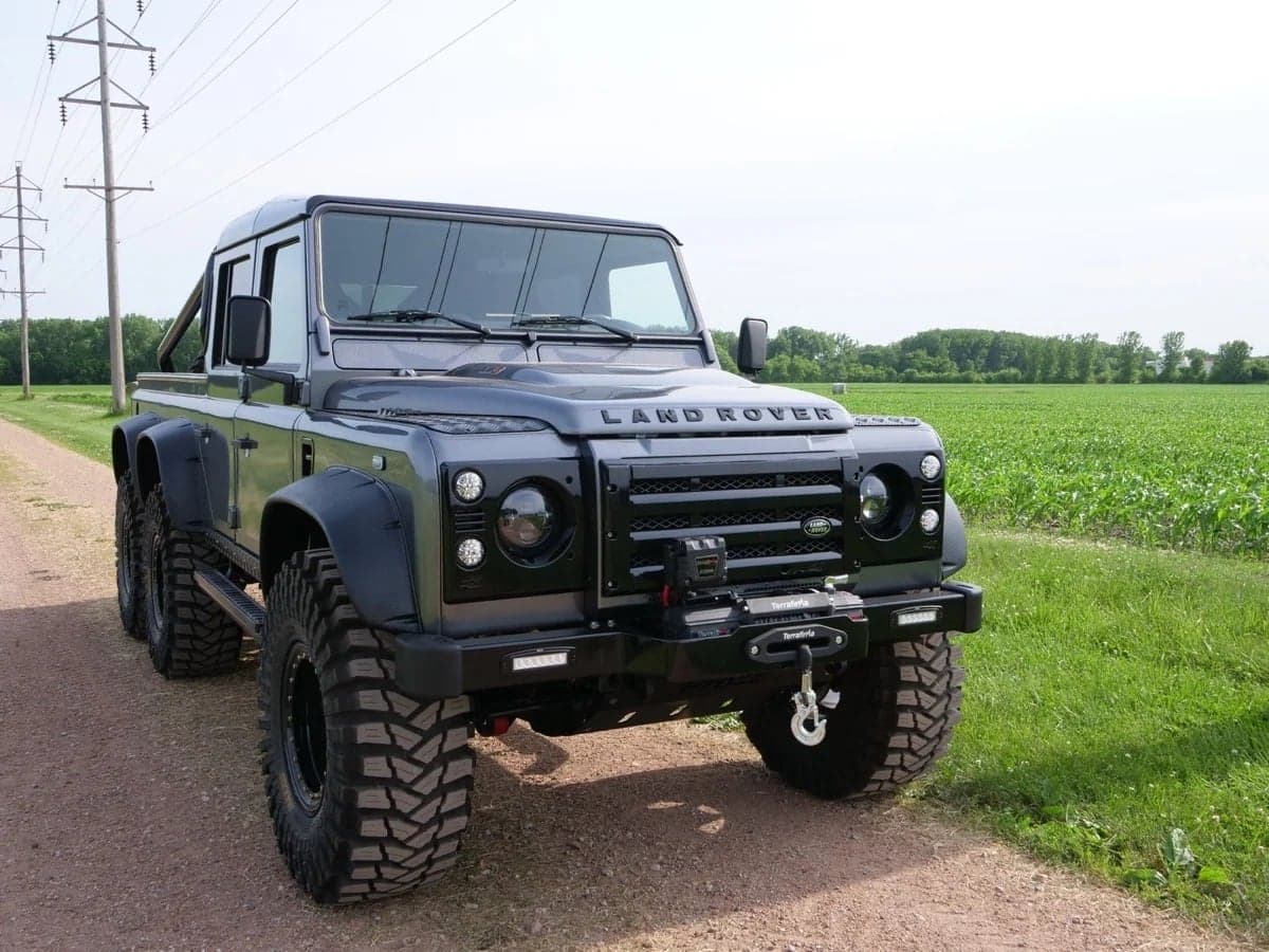 Front View: Custom Land Rover Defender Black modified Land Rover Defender parked on a dirt road with lush green fields in the background