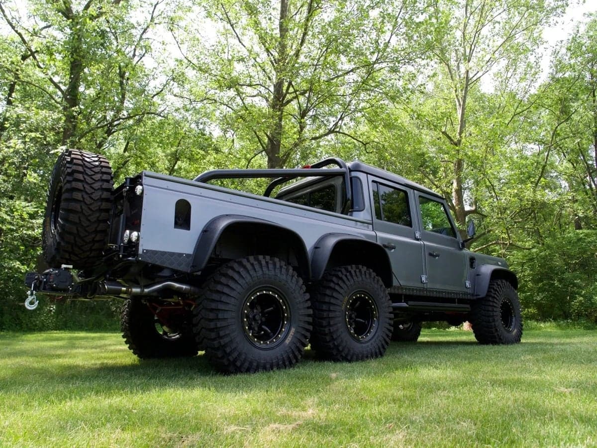 Side View: Bespoke Land Rover Defender Custom Land Rover Defender in grey with large off-road tires parked in a grassy area