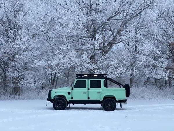 Side View: Custom Land Rover Defender A mint green custom Land Rover Defender parked in a snowy landscape with frosted trees in the background