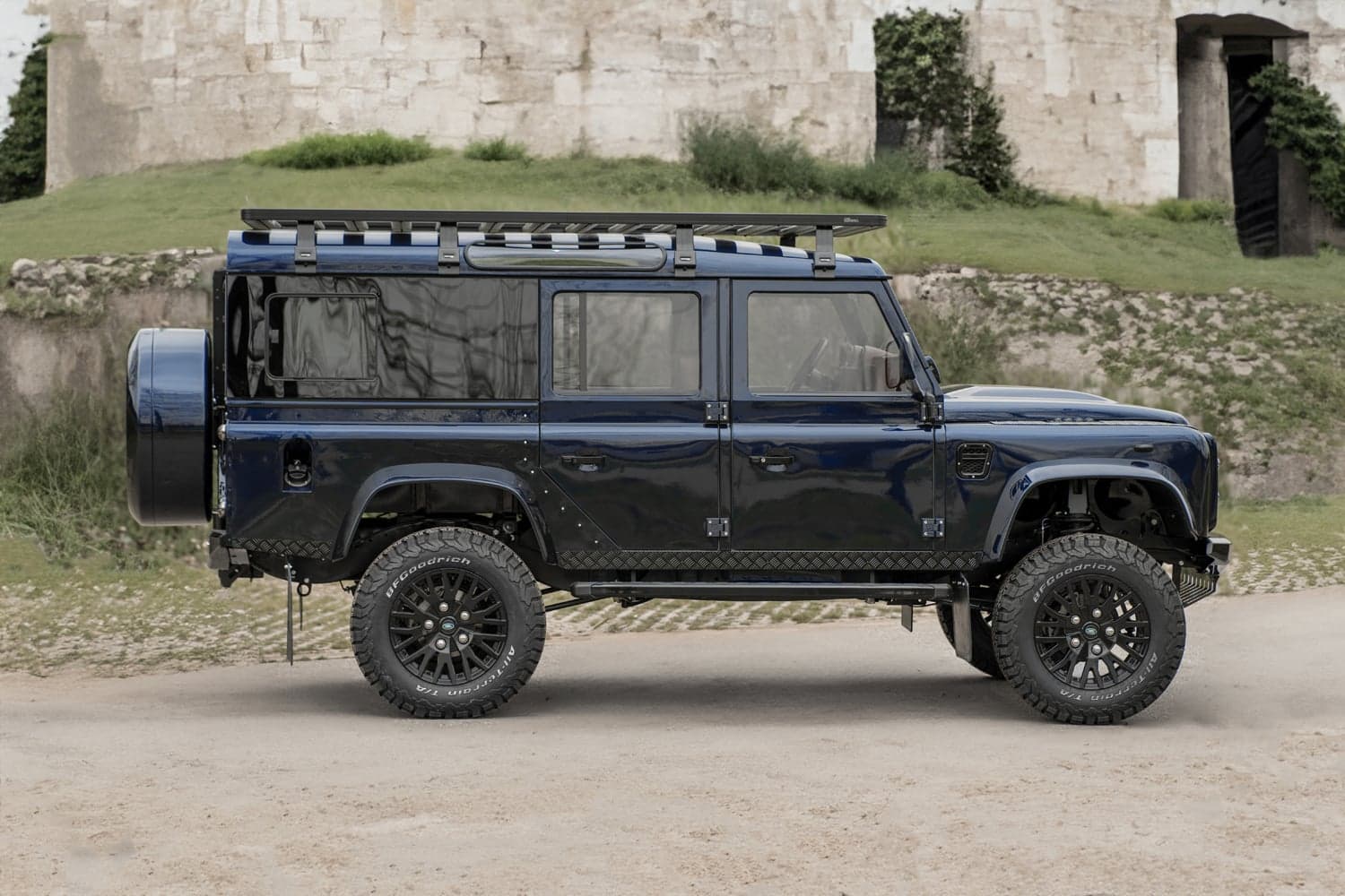 Side View: Bespoke Land Rover Defender Custom blue Land Rover Defender parked on dirt with rugged terrain