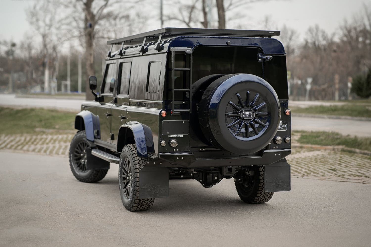 Rear View: Bespoke Land Rover Defender Rear view of a luxury custom Land Rover Defender in deep blue with off-road tires and roof rack