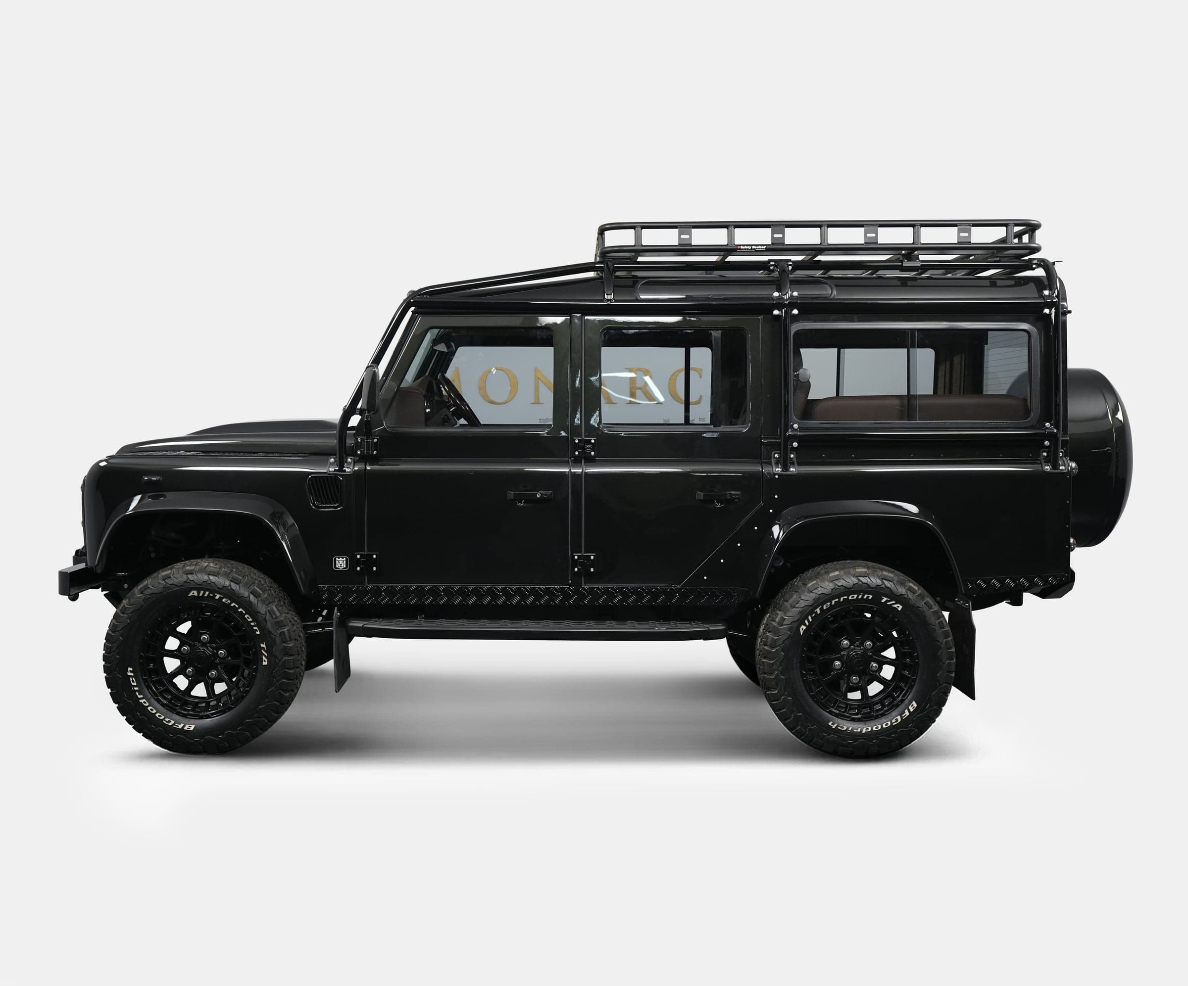 Side View: Custom Land Rover Defender Side view of a bespoke black Land Rover Defender with off-road tires and a roof rack